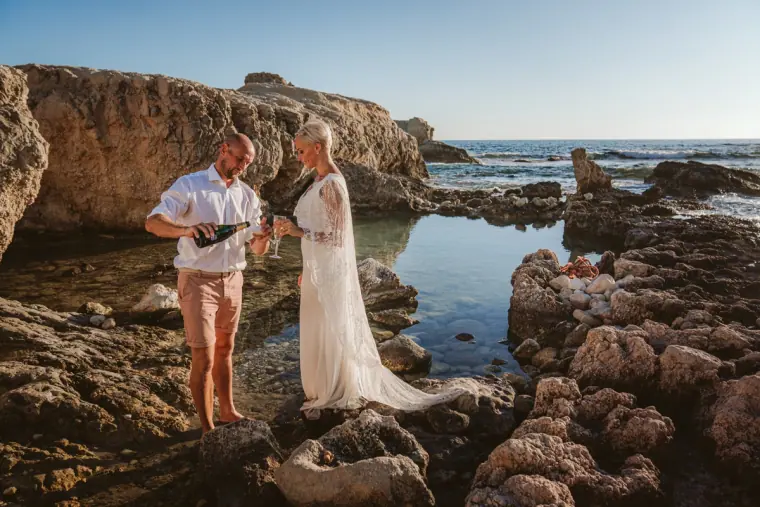 Luke spraying champagne as Alana laughs among the rock pools