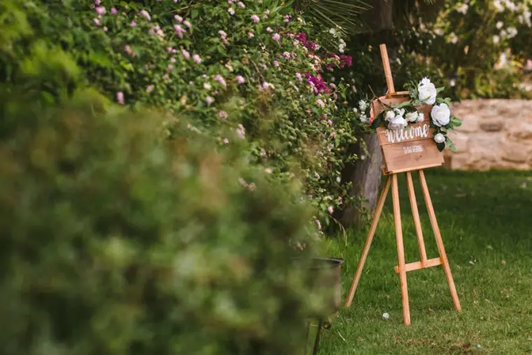 Wooden easel with a floral welcome sign in a garden of flowering shrubs