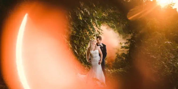 Bride and groom framed within a glowing ring of orange light flare