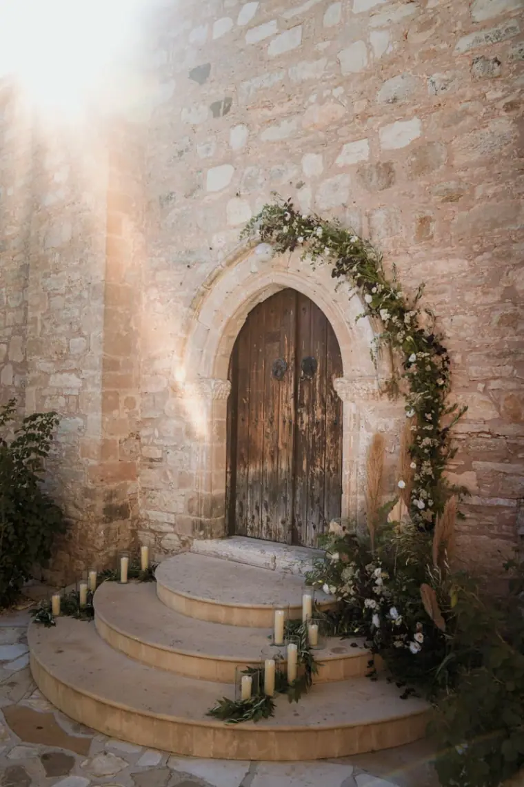 Arched wooden chapel door with an ivy garland and candles on the steps
