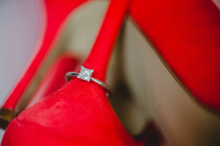 Diamond engagement ring balanced on the heel of a red shoe