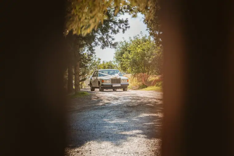 Vintage wedding car arriving down a gravel drive, seen through a doorway
