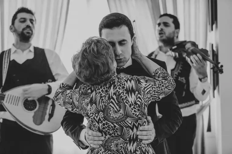 Black-and-white photo of the groom hugging a relative as musicians play