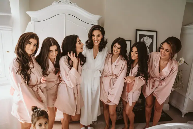 Bride in a white robe with bridesmaids in matching pink robes laughing together