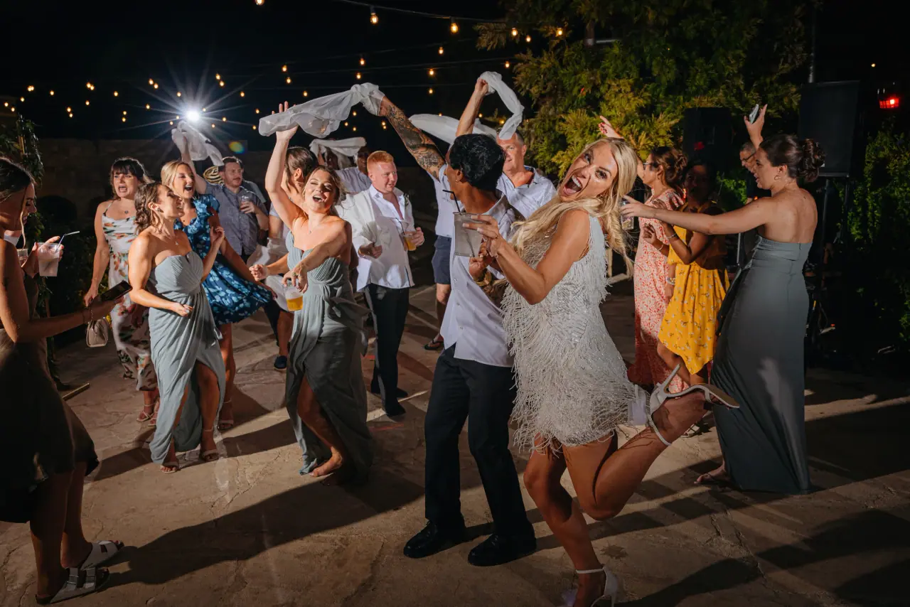 Guests waving napkins and dancing under string lights at Emma and Aaron's Liopetro reception