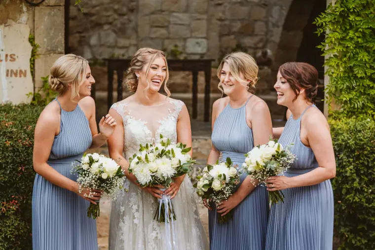 Bride with three bridesmaids in dusty blue dresses holding white bouquets