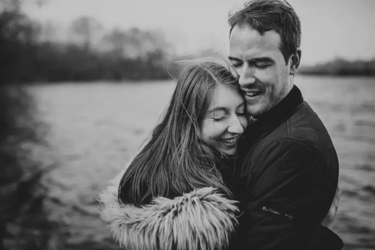 Black-and-white photo of the couple cuddling and laughing by the lake
