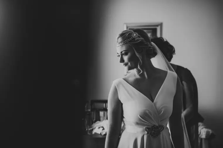 Black-and-white portrait of the bride looking down as her veil is fitted