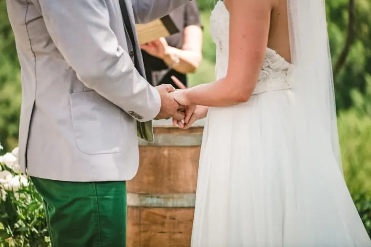 Close-up of the bride and groom holding hands beside a wine barrel during the ceremony