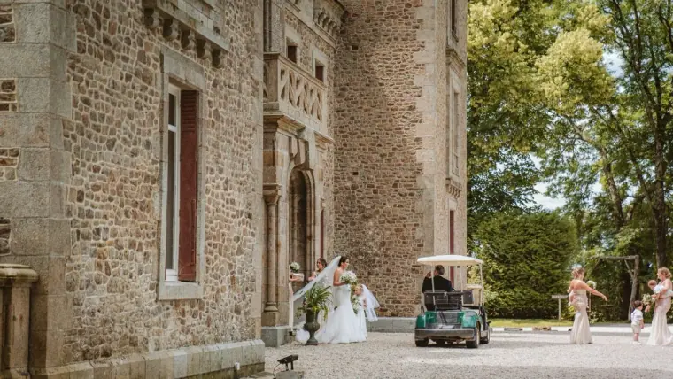 Bride arriving by golf buggy beside the stone walls of the château
