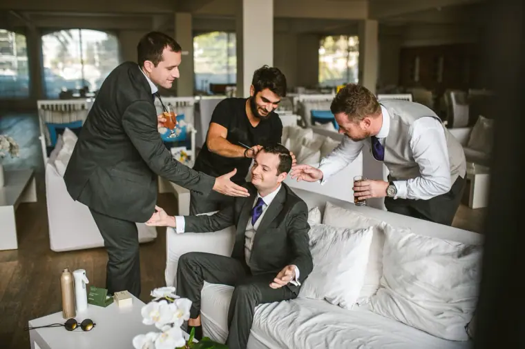 Groom laughing with friends as they help him get ready in a hotel lounge