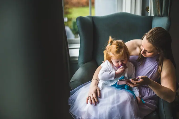 Woman in a lilac dress holding a toddler in a tulle dress on an armchair