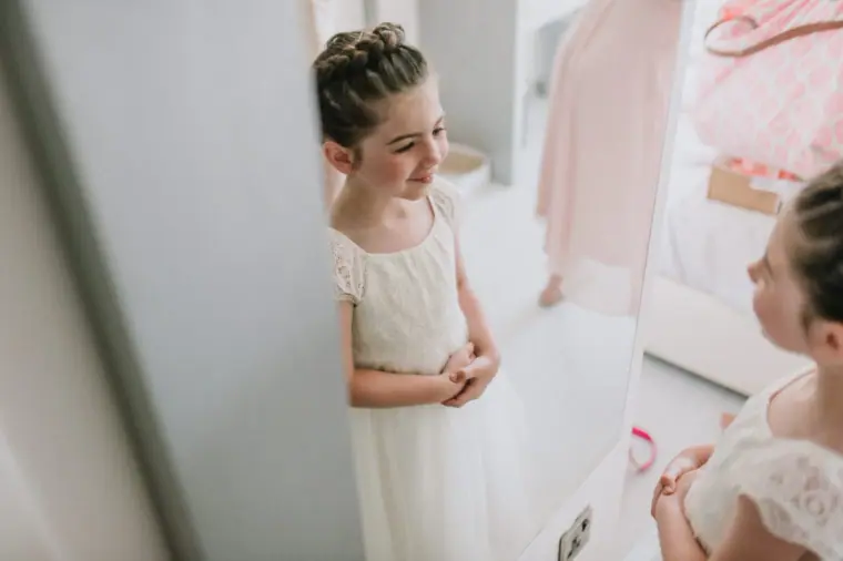 Flower girl in a cream dress standing in the hotel room