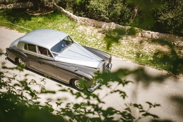 Silver vintage Rolls-Royce wedding car on a tree-lined driveway
