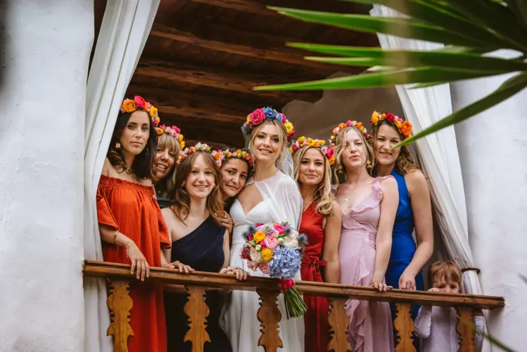 Bridesmaids in flower crowns and colourful dresses on a balcony with the bride