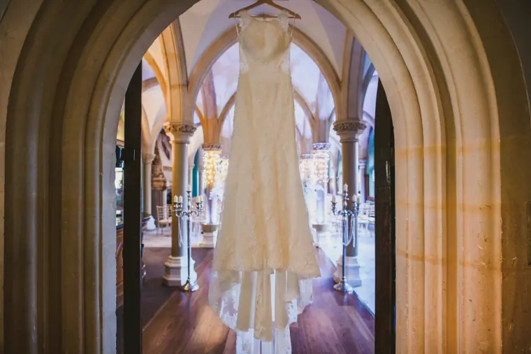 Wedding dress hanging in a Gothic stone archway with a vaulted corridor beyond