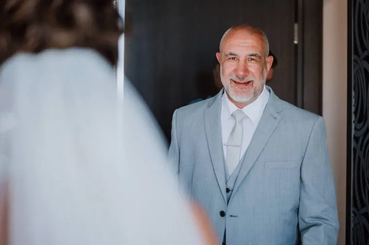 Father of the bride in a grey suit smiling as he sees his daughter