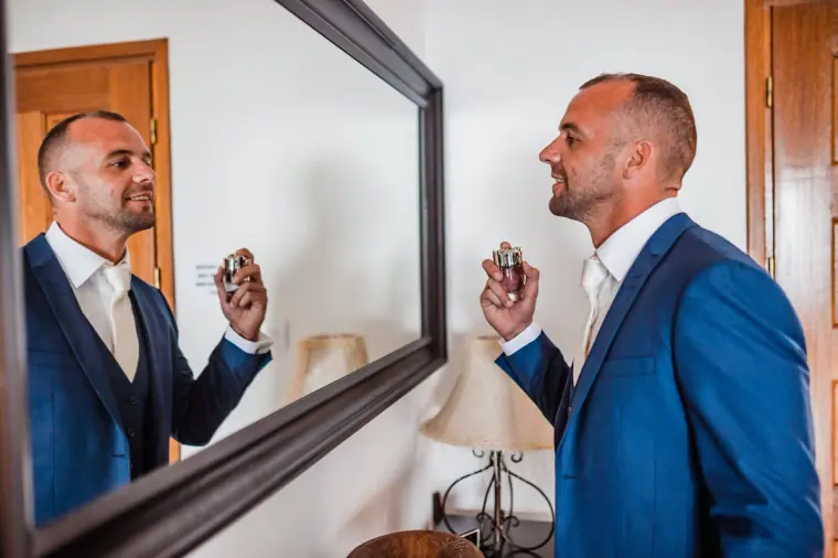 Groom spraying aftershave in front of a mirror, dressed in a navy suit