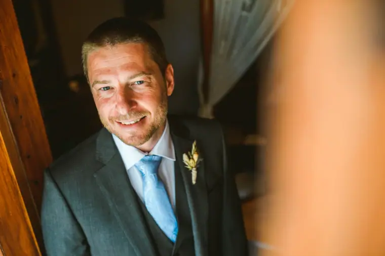 Kazem smiling in his grey suit and blue tie, framed by a wooden door