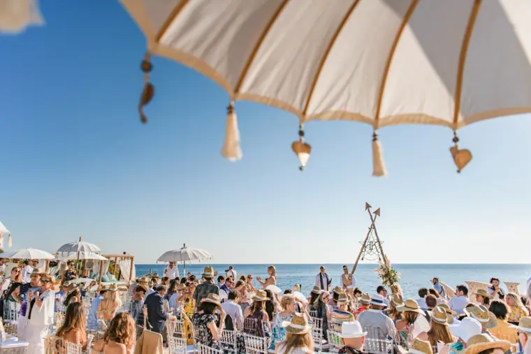 Guests seated beneath tasselled parasols for the ceremony by the sea