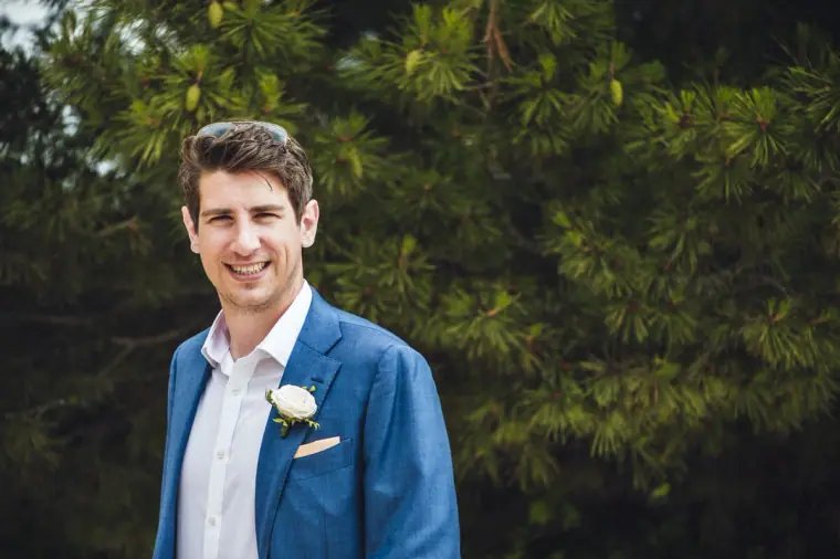 Paul in a blue suit with a white buttonhole, smiling among pine trees