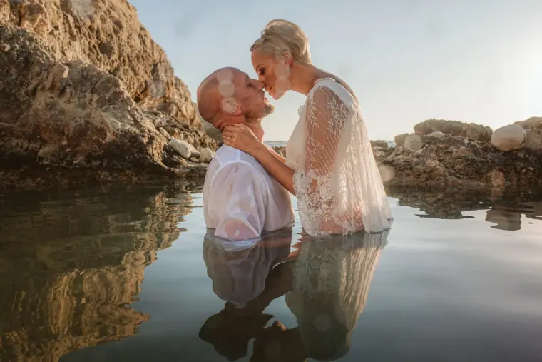Alana and Luke kissing in the water with a sea cave behind them
