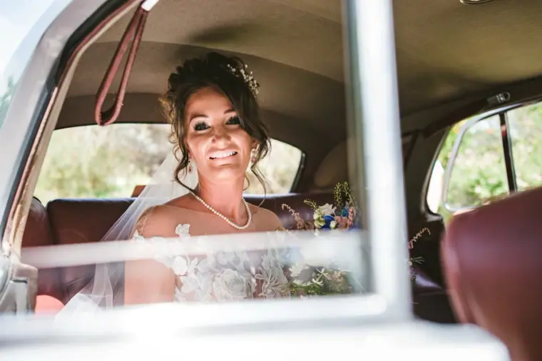 Amie smiling from the back seat of the vintage wedding car