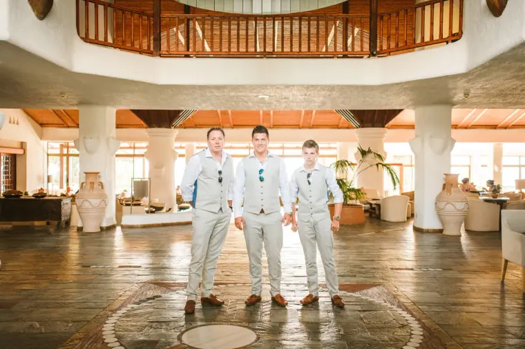 Groom and two groomsmen standing in the grand lobby of Coral Beach Hotel, Paphos