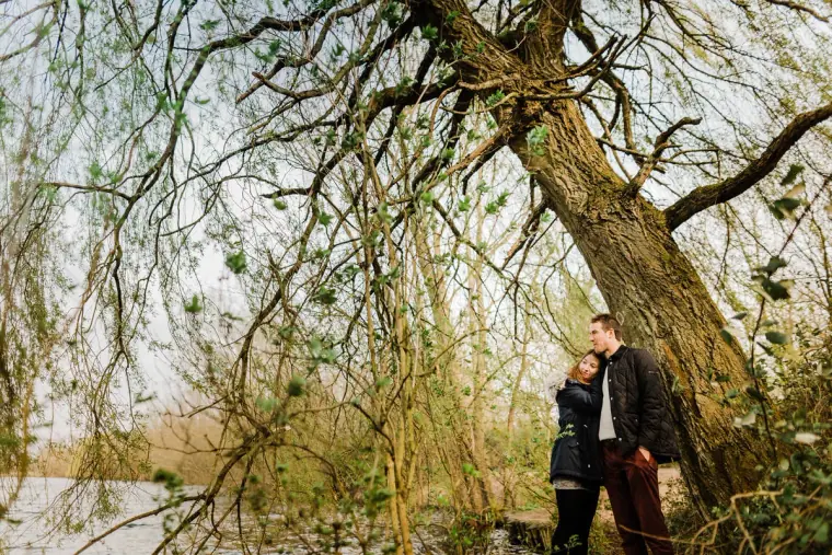 Couple standing beneath a large willow tree by the lake