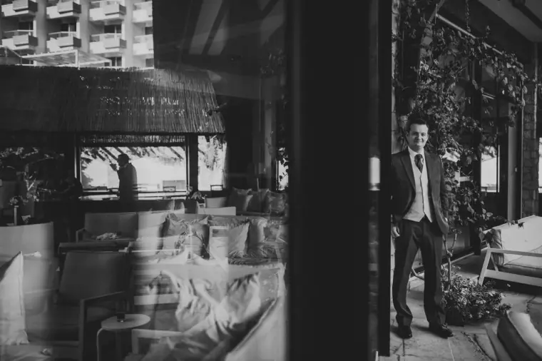 Black-and-white photo of the groom standing by a window in a hotel lounge