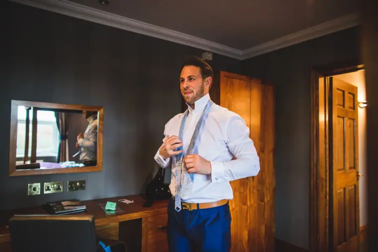 Groom adjusting his tie in front of a mirror in his hotel room