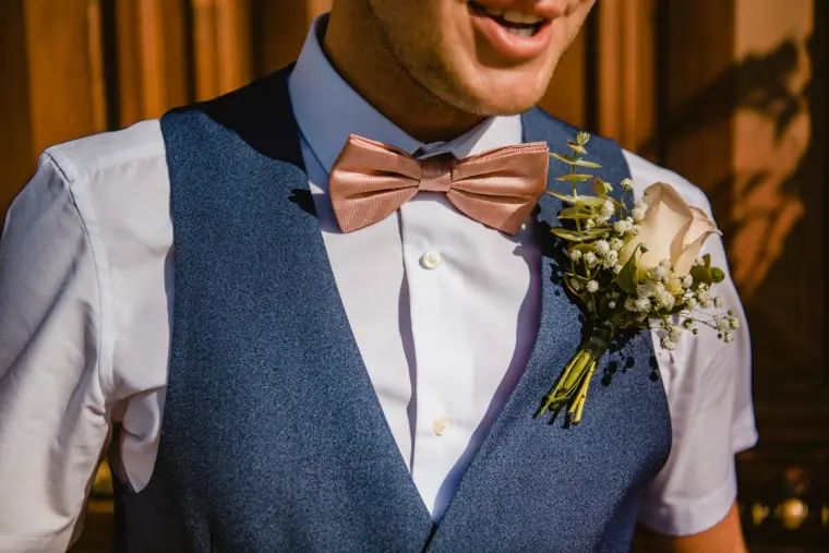 Close-up of the groom's pink bow tie, navy waistcoat and buttonhole