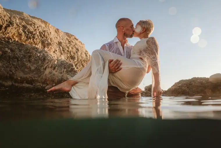 Luke carrying Alana in the shallows beside the rocks near Paphos