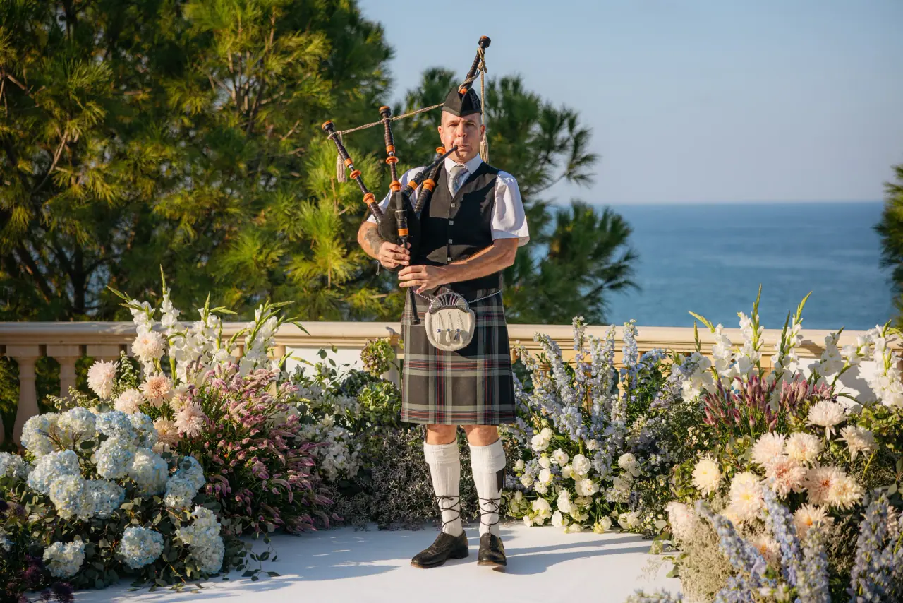 Bagpiper in a kilt on a floral aisle above the sea at Anassa