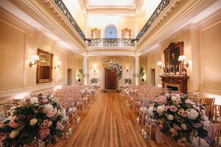 Grand ceremony hall at Hedsor House with chairs, chandeliers and pink floral aisle arrangements