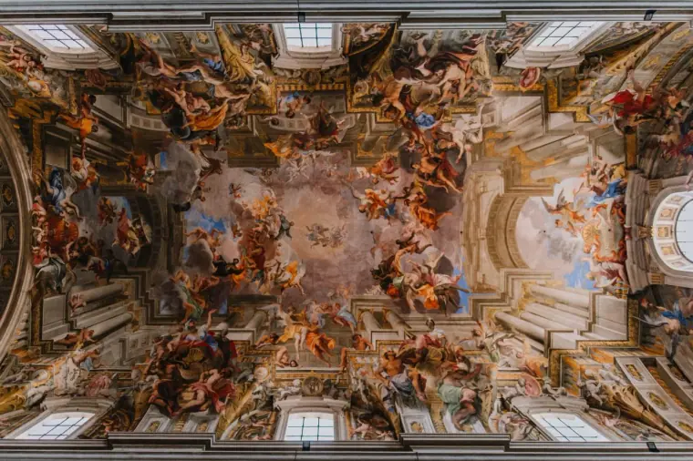 Looking up at a richly painted Baroque church ceiling with gilded details in Rome