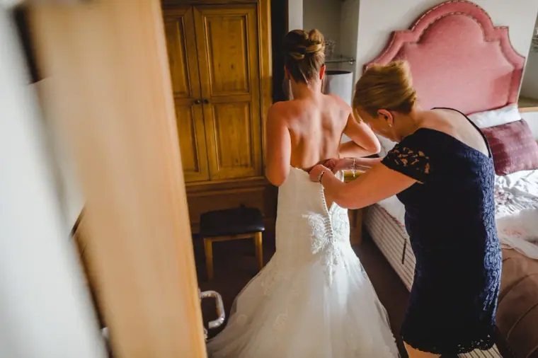 Bride being laced into her gown by a woman in a navy lace dress