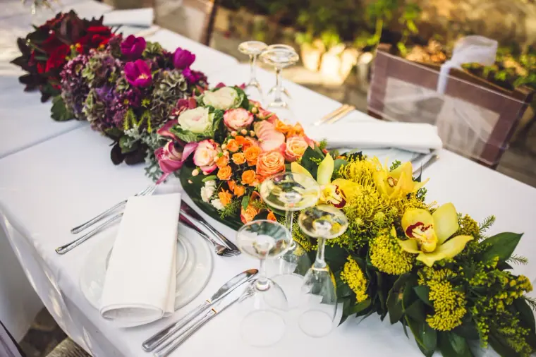 Long table runner of orchids, roses and yellow flowers on a white tablecloth