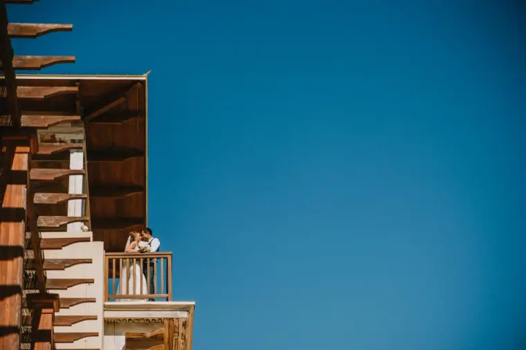 Danielle and Aaron on a timber balcony under a clear blue sky at Elea Estate, Paphos