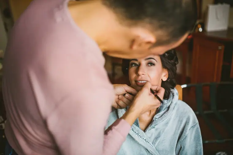 Make-up artist applying the bride's lipstick by the window