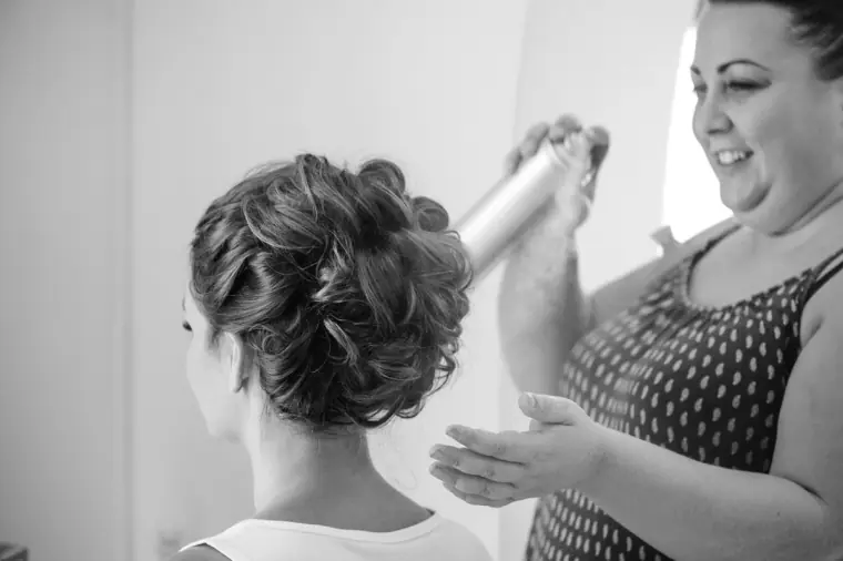 Black-and-white photo of the hairdresser spraying the bride's updo