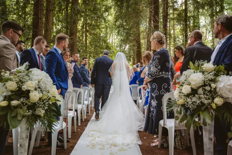 Bride walking down a petal-strewn aisle between guests in the forest