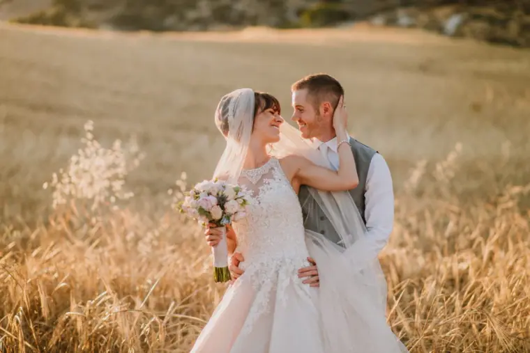 Bride and groom smiling at each other among sunlit golden grasses near Vasilias Inn, Kouklia