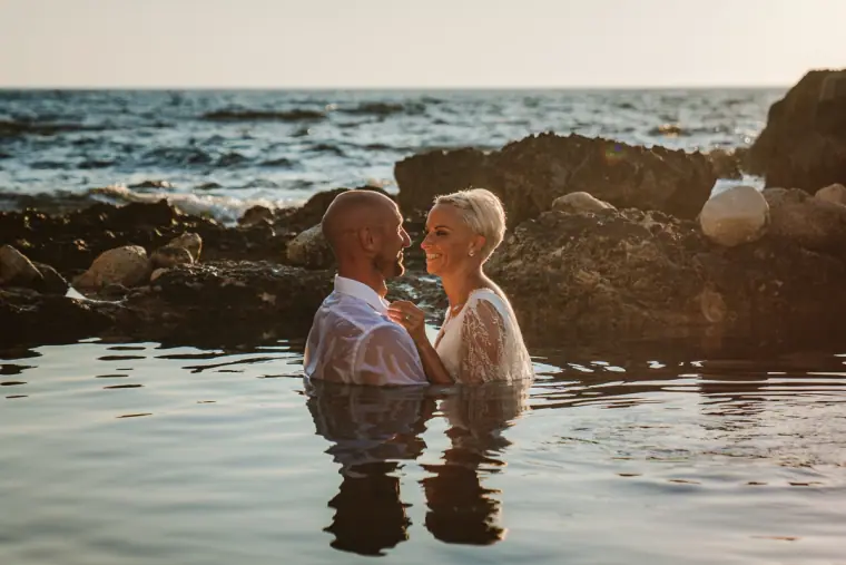 Couple standing chest-deep in the sea, toasting with champagne