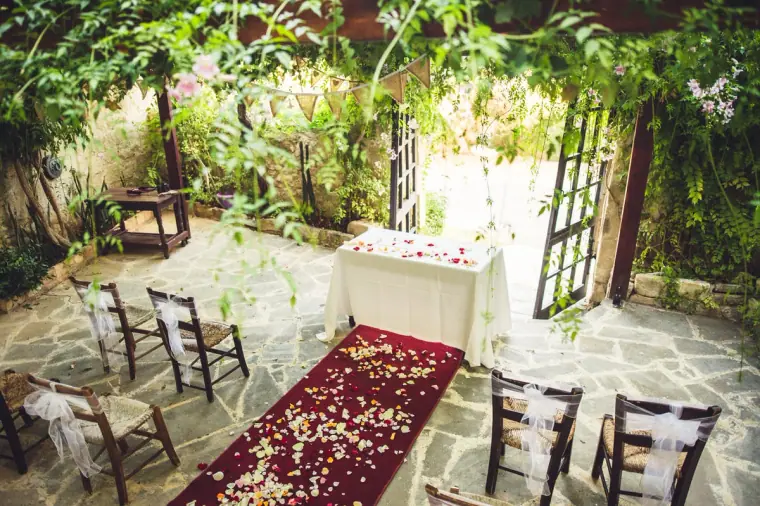 Ceremony table at the end of a red petal-strewn aisle under the vine-covered pergola