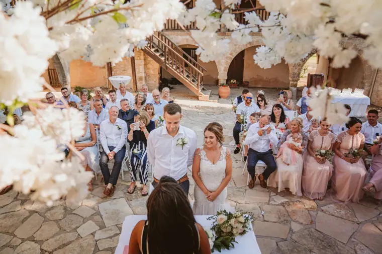 Groom watching his bride approach the ceremony, seen through white blossoms