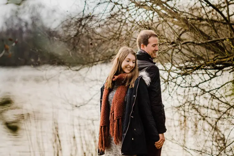 Jana in a red scarf standing close to Alex by the lake
