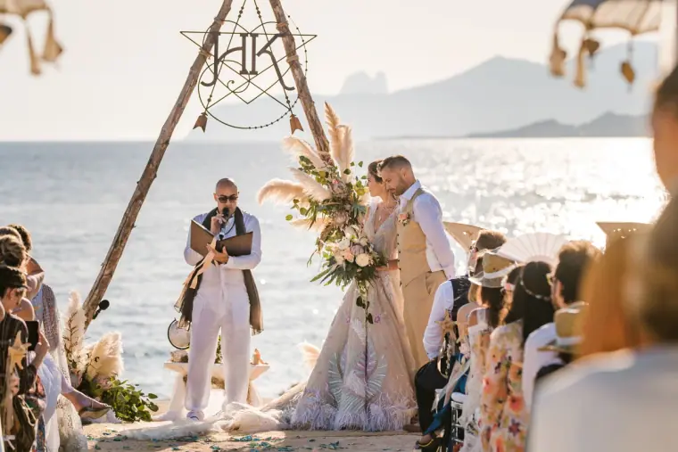 Kenton and Hassiba facing the celebrant under the tipi arch, sea behind