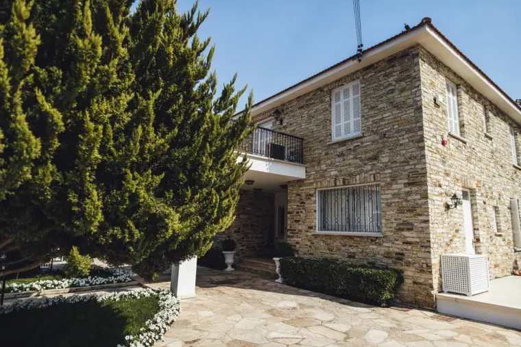 Stone house with tall conifer trees under a blue sky in Nicosia