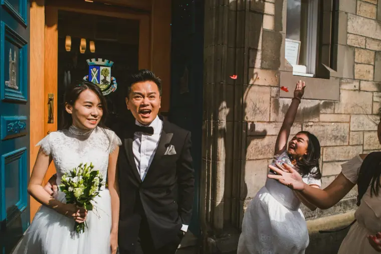 Couple leaving a stone church door as a guest throws confetti in St Andrews, Scotland